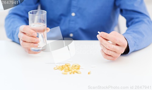 Image of male hand holding pill and glass of water