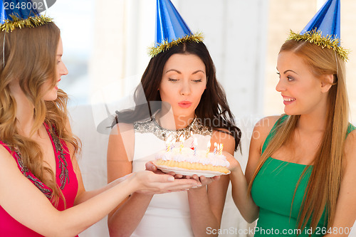 Image of three women wearing hats holding cake with candles