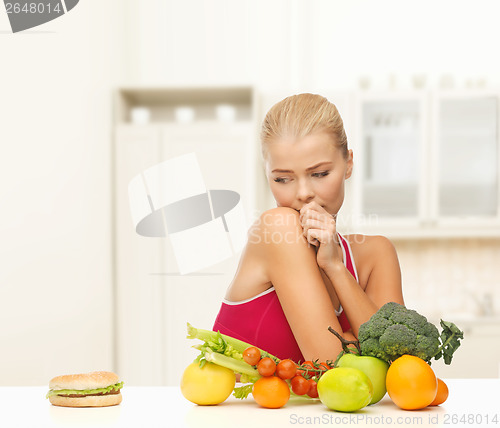 Image of doubting woman with fruits and hamburger