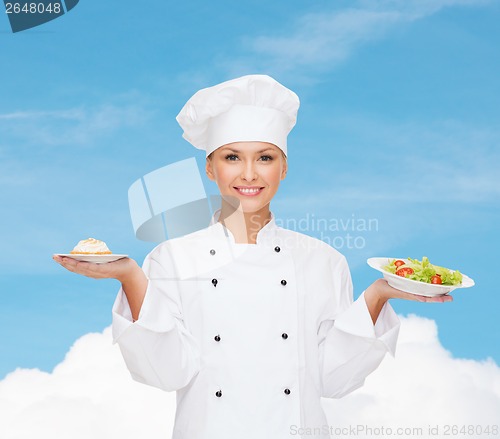 Image of smiling female chef with salad and cake on plates