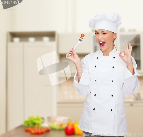 Image of smiling female chef with fork and tomato