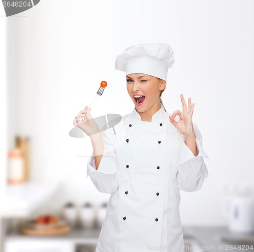 Image of smiling female chef with fork and tomato