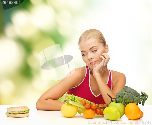 Image of doubting woman with fruits and hamburger