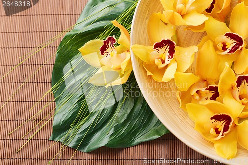 Image of orchid flowers in bowl with green leaf on mat
