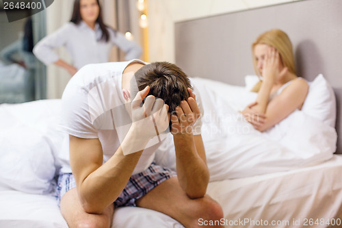 Image of man sitting on the bed with two women on the back