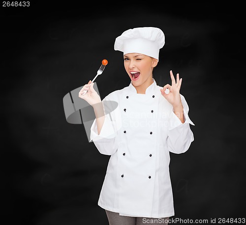 Image of smiling female chef with fork and tomato