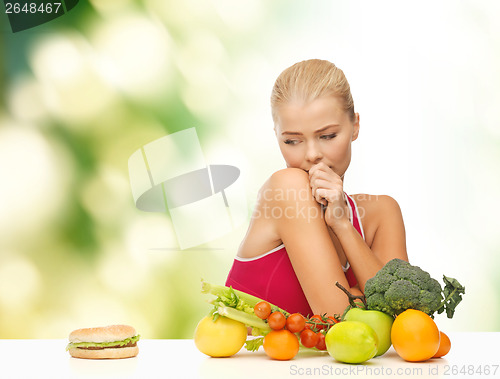 Image of doubting woman with fruits and hamburger