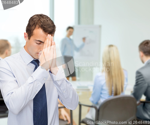 Image of praying young buisnessman at office