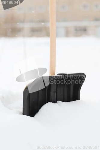 Image of black snowshowel with wooden handle in snow pile