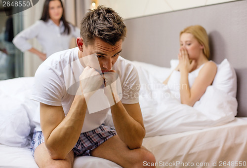 Image of man sitting on the bed with two women on the back