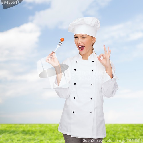 Image of smiling female chef with fork and tomato