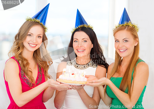 Image of three women wearing hats holding cake with candles