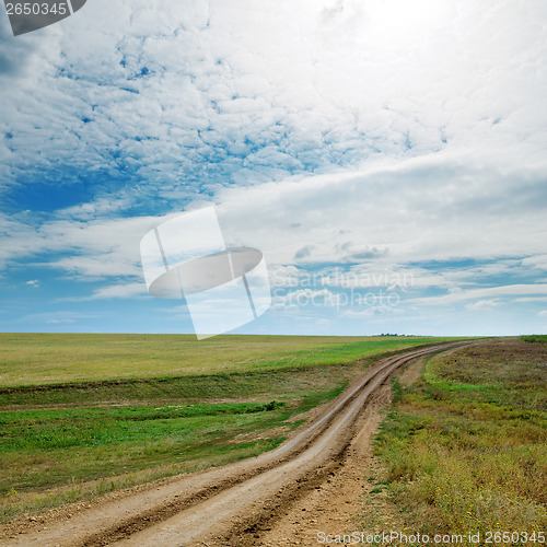 Image of rural road in green fields and cloudy sky