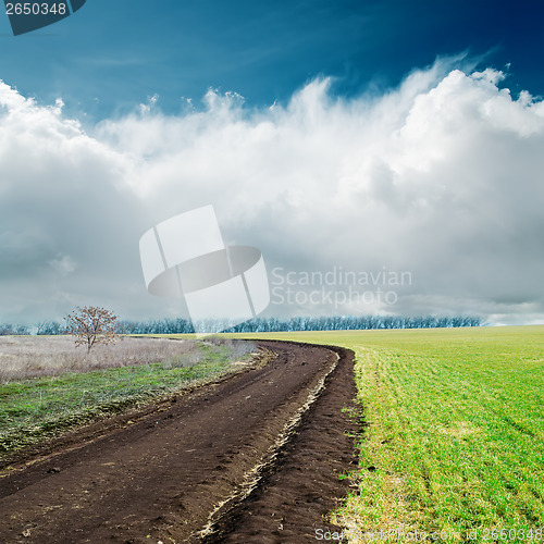 Image of spring dirty road in green fields and clouds over it