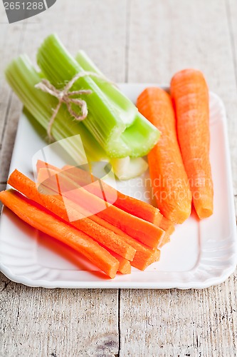 Image of bundle of fresh green celery stems and carrot in plate