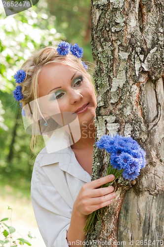 Image of Woman with blue flowers peeking from behind a tree