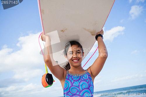 Image of Happy young girl holding surfboard on head