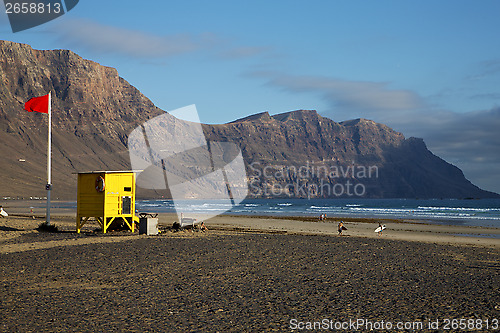 Image of lifeguard chair red flag in s  rock stone sky cloud beach  pond 