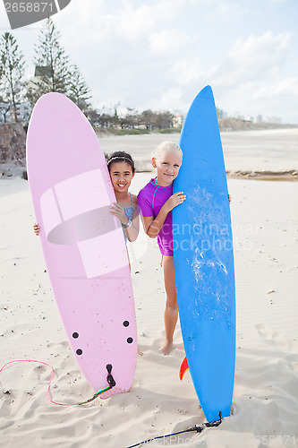 Image of Two happy young girls holding surfboards at beach