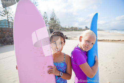 Image of Two happy young girls holding surfboards at beach