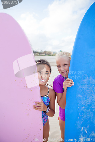 Image of Two happy young girls holding surfboards at beach