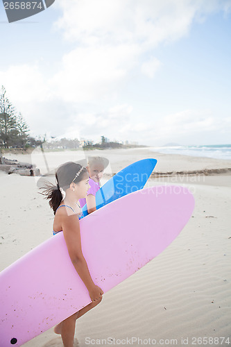 Image of Two cute young girls walking together with surfboards at beach