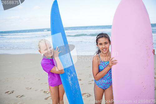 Image of Two happy young girls holding surfboards at beach