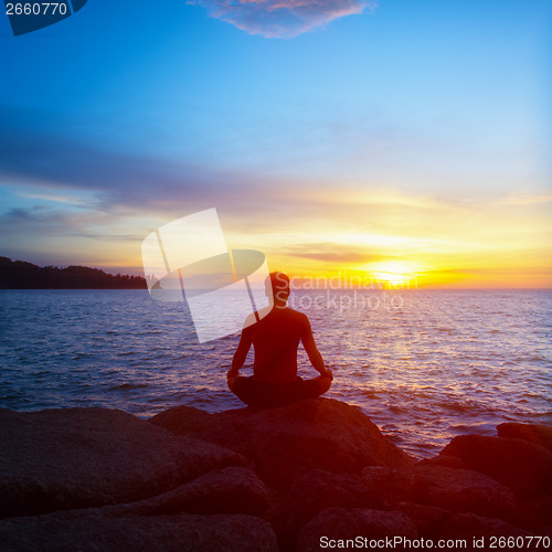 Image of Young man practices yoga on the beach at sunset