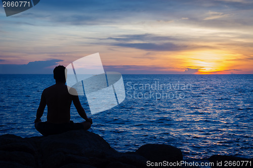 Image of Young man practicing yoga on ocean shore