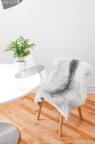 Image of Chair covered with sheepskin, and plant on a white table