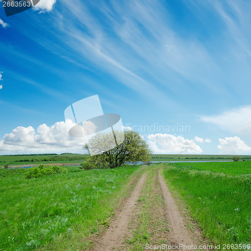 Image of dirty road in green field and blue sky with clouds