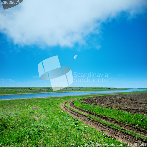 Image of green field and road under cloudy sky in evening