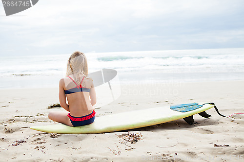Image of Young girl sitting on surfboard on beach