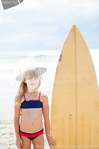 Image of Smiling young girl standing next to surfboard