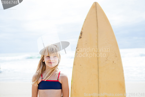 Image of Smiling young girl standing next to surfboard