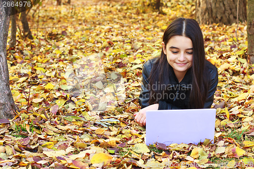 Image of Teenager laying on leaves with laptop