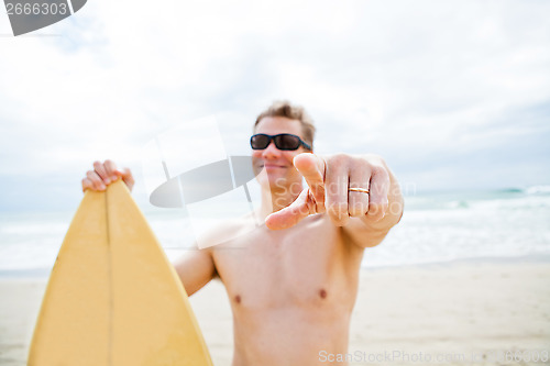 Image of Smiling man with surfboard at beach pointing with finger