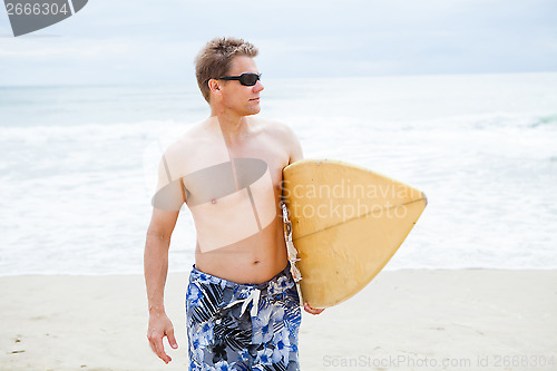 Image of Relaxed looking man walking with surfboard at beach