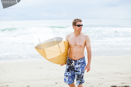 Image of Serious looking man walking with surfboard at beach