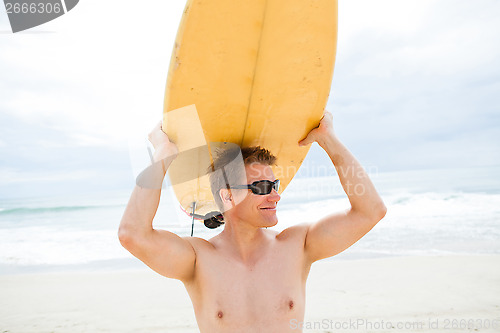 Image of Smiling man resting surfboard on head at beach