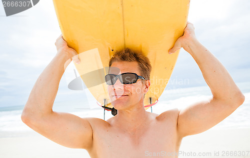 Image of Smiling man resting surfboard on head at beach