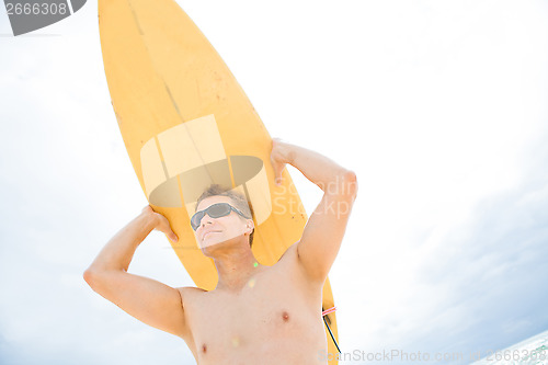 Image of Man resting surfboard on head at beach