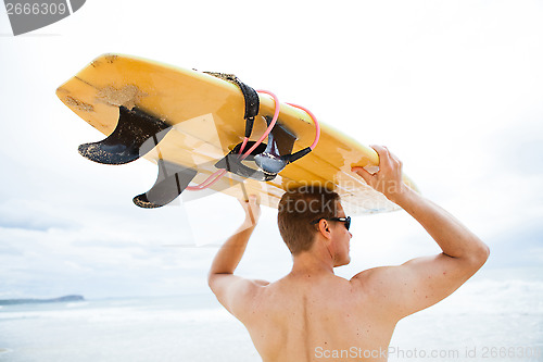 Image of Man resting surfboard on head at beach