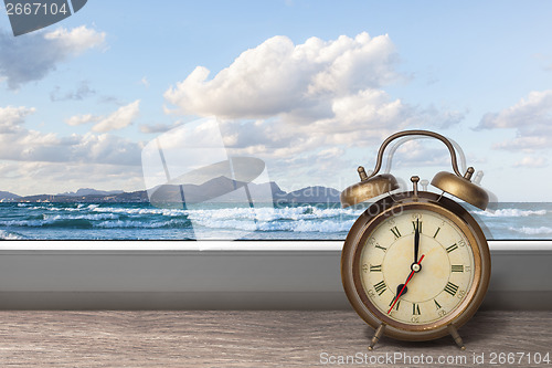Image of View of summer sea under blue sky from window with alarm clock