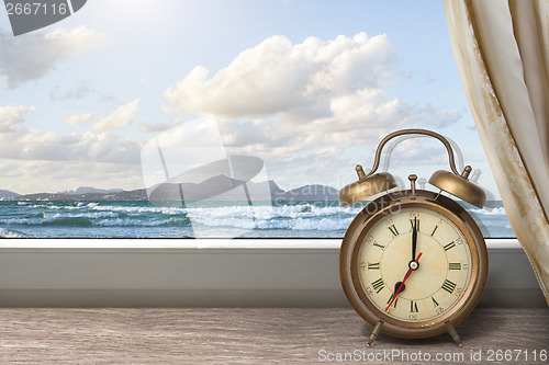 Image of View of summer sea under blue sky from window with alarm clock