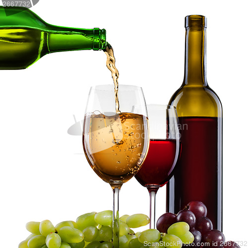 Image of White wine pouring into glass with grape and bottles isolated