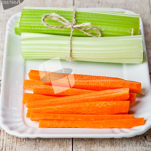 Image of bundle of fresh green celery stems and carrot in plate