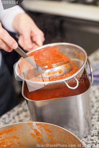 Image of Woman chef whisking boiled tomato sauce in a pot
