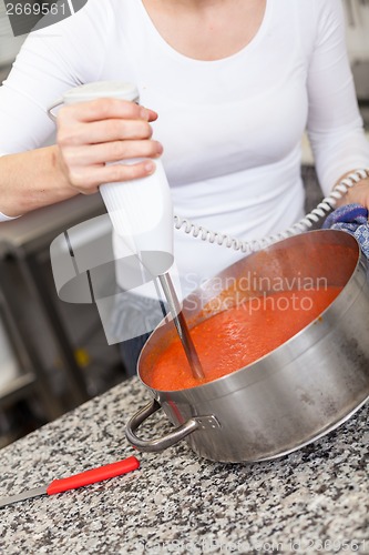 Image of Woman chef whisking boiled tomato sauce in a pot
