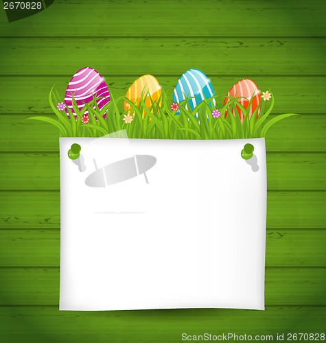 Image of  Easter colorful eggs in green grass with empty paper card for y